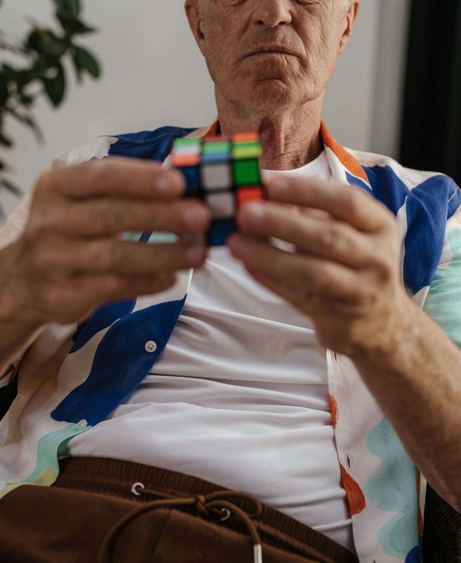 Elderly man focusing on solving a Rubik's Cube indoors, demonstrating concentration and puzzle-solving skills.